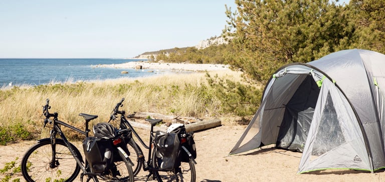 Två cyklar utanför ett grått tält i skogsbryn vid stranden